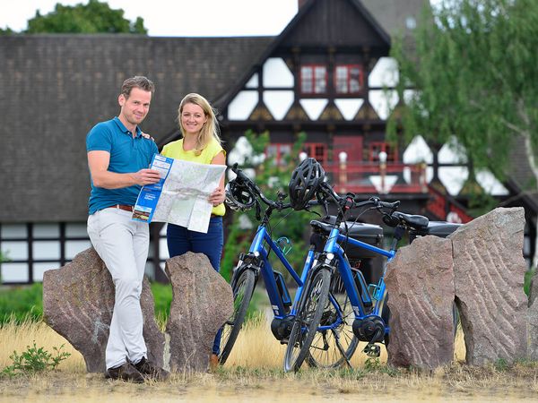 Ein Mann und eine Frau stehen mit zwei Fahrrädern und einer Radkarte in der Hand im Schlosspark in Gifhorn.