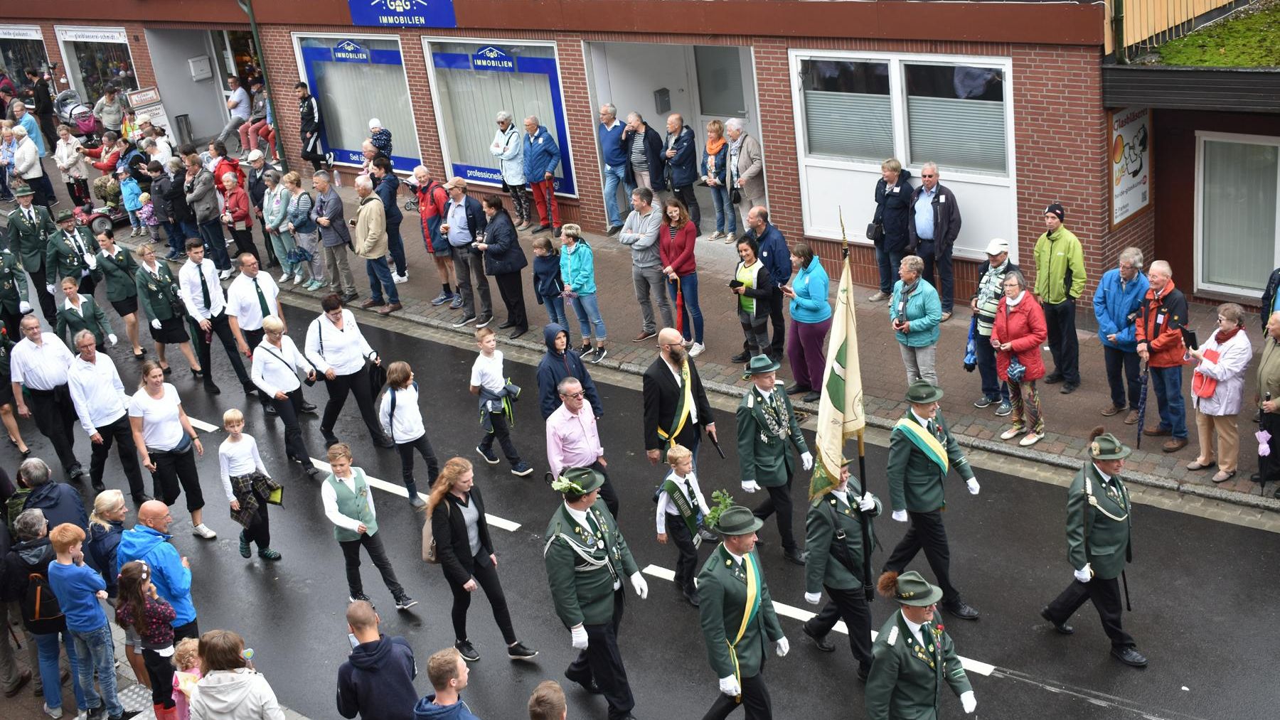 „Menschenmenge bei einem Festumzug durch eine Straße mit Fachwerkhäusern in Amelinghausen. Musikkapelle in Uniform läuft voran.“