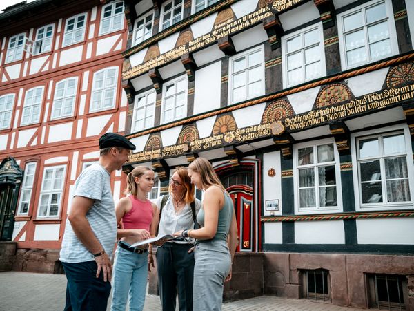 Eine Familie steht vor einem Fachwerkhaus und sieht sich eine Broschüre an.