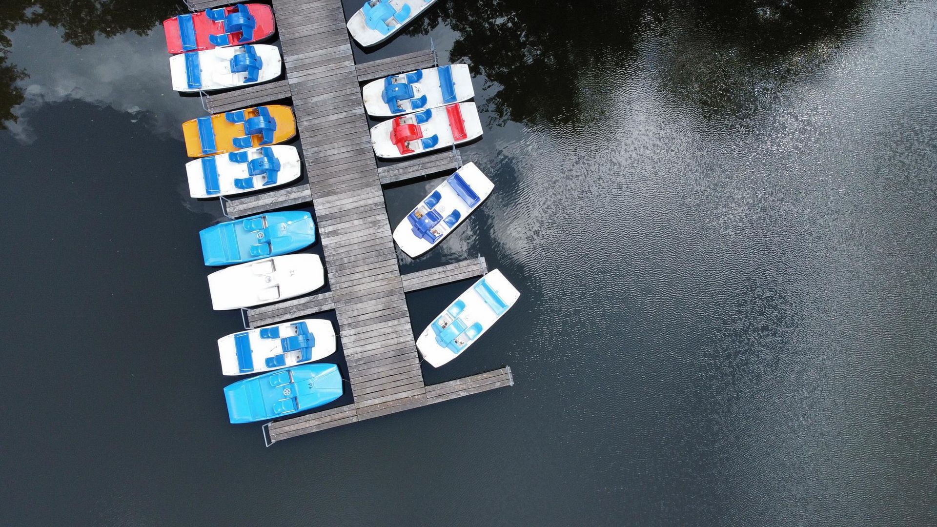 „Luftaufnahme eines Stegs mit bunten Tretbooten auf ruhigem Wasser“