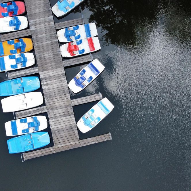 Lopausee Amelinghausen „Luftaufnahme eines Stegs mit bunten Tretbooten auf ruhigem Wasser“